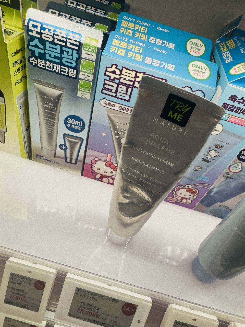 S.NATURE Aqua Squalane Moisturizing Cream tube held at an Olive Young shelf in Seoul, with the Olive Young Awards badges and electronic price labels visible